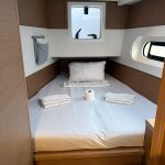 Cabine avant du catamaran Excess 12 avec lit double, hublots panoramiques et rangements pour une croisière aux Grenadines.
